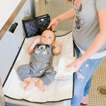 Disney Baby Full Body Changing Pad, Mickey Black unfolded on bathroom changing table with baby on it