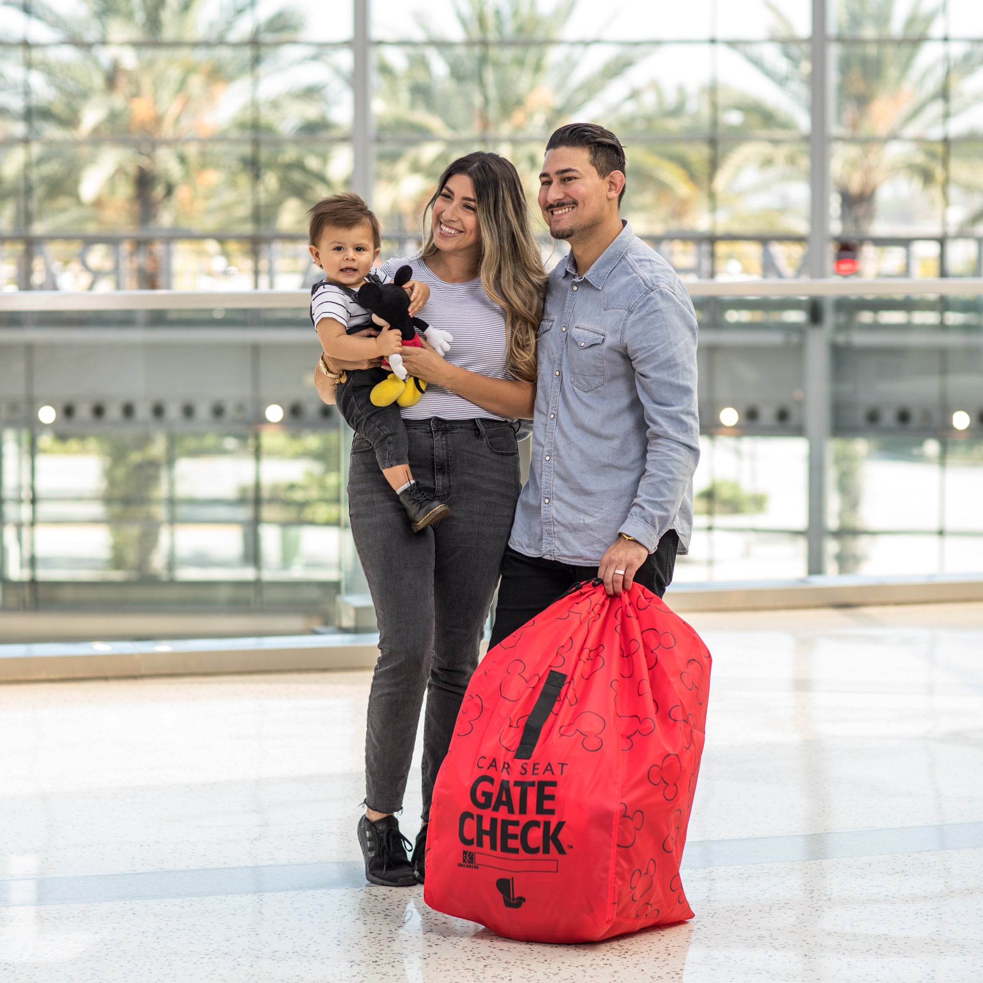 Family standing next to the Disney Baby Gate Check Travel Bag for Car Seats