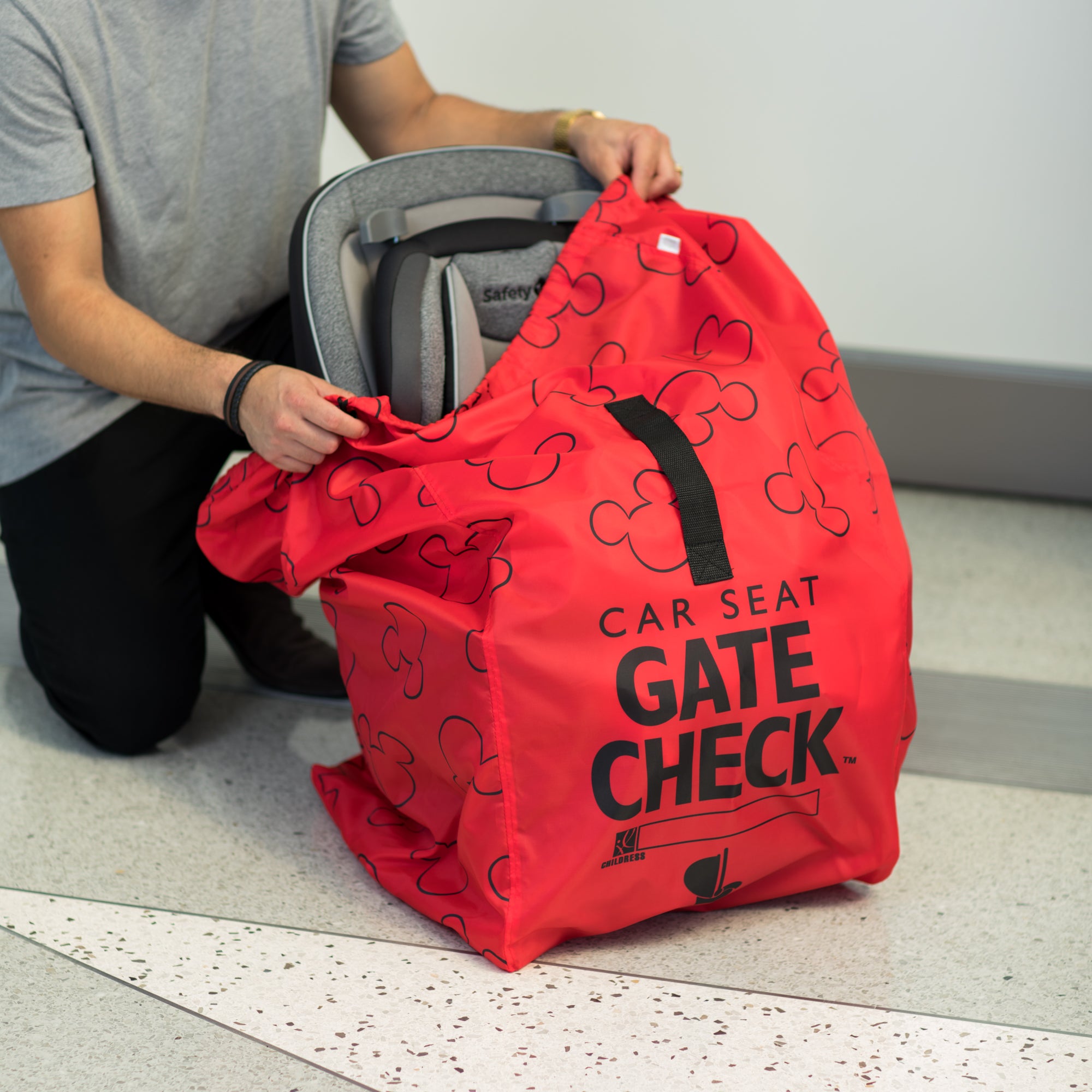 Man putting car seat in the Disney Baby Gate Check Travel Bag for Car Seats