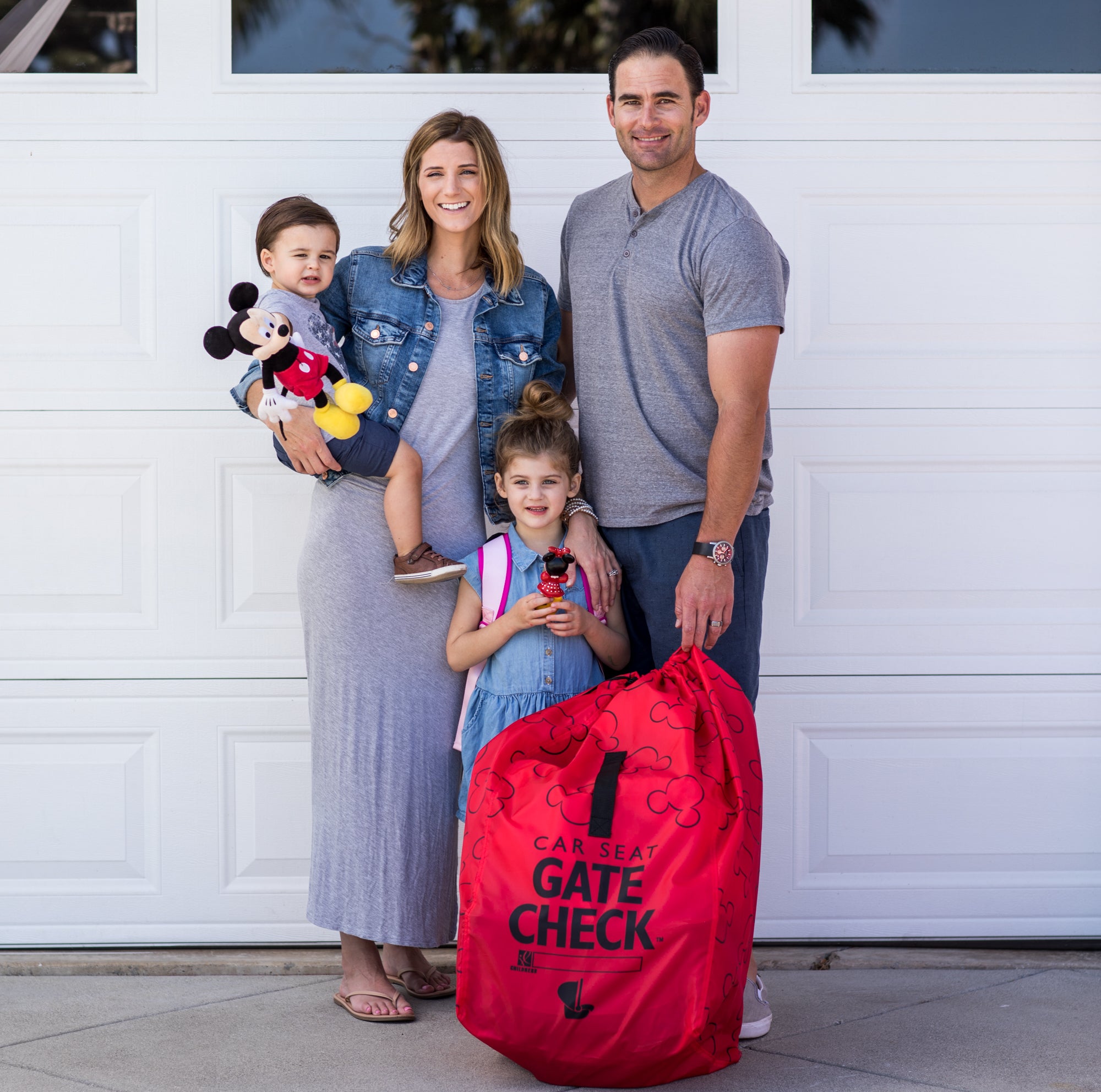 Family standing next to the Disney Baby Gate Check Travel Bag for Car Seats