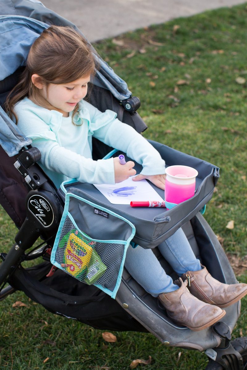 Child sitting in stroller with the 3-IN-1 Travel Tray and Tablet Holder placed on their lap and drawing on it