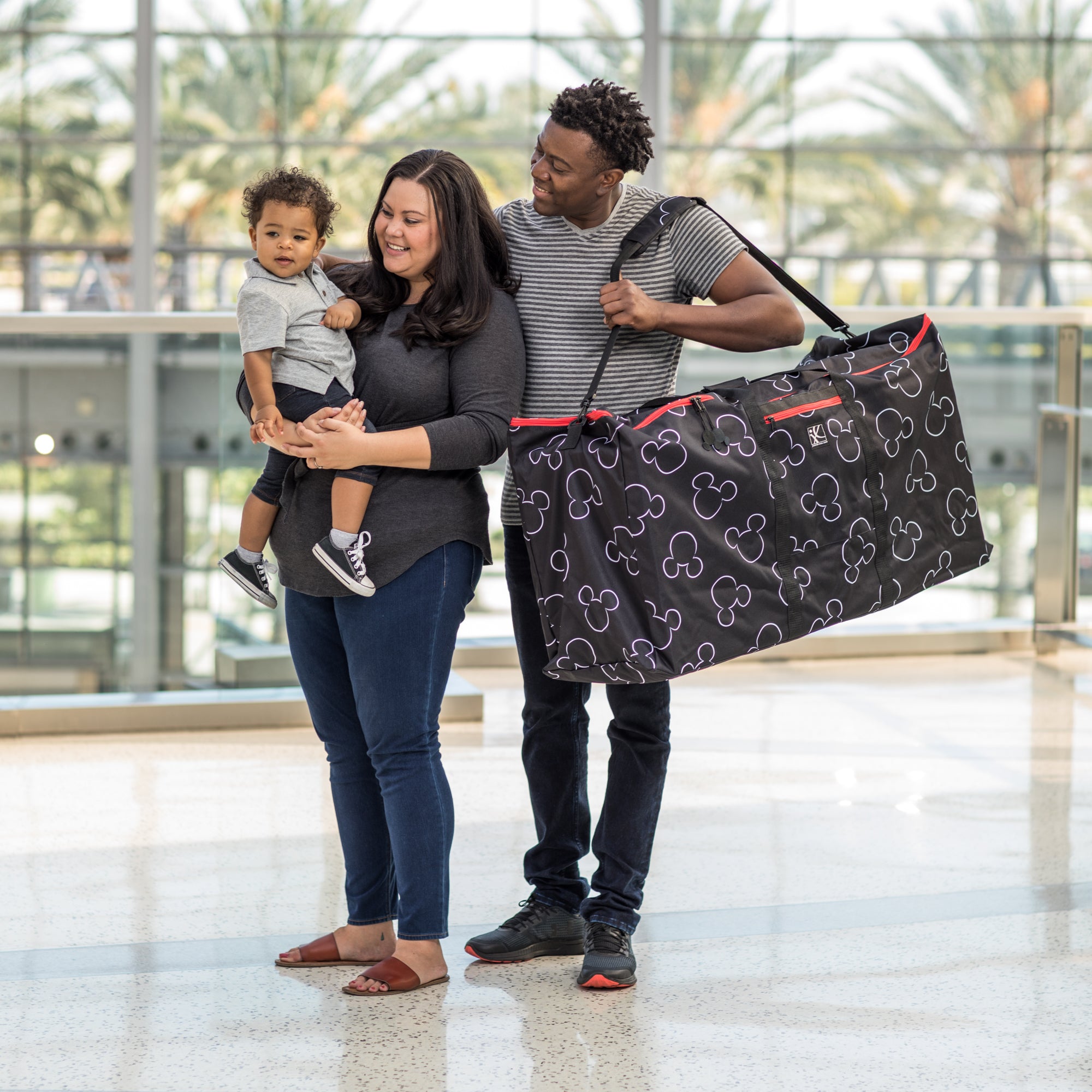 Woman holding baby with man carrying the Disney Baby Single & Double Stroller Travel Bag, Mickey Black