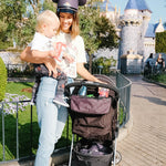 Woman holding baby standing next to stroller with Disney Baby Universal Stroller Organizer hanging on it